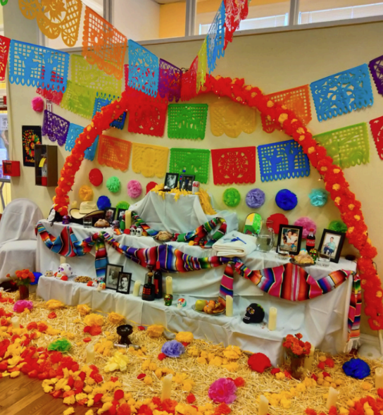 A Day of the Death altar with marigolds, candles, food, and framed photos.